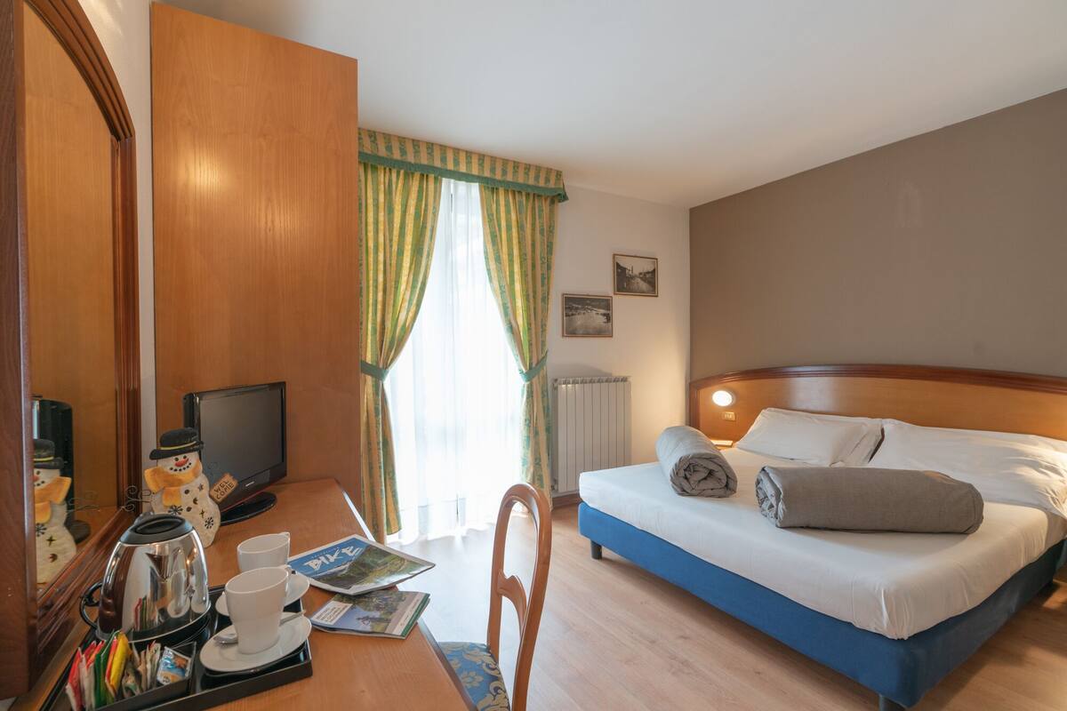 Una habitación de hotel con una cama, un escritorio con cafetera, tazas y una bandeja con alimentos para el desayuno.