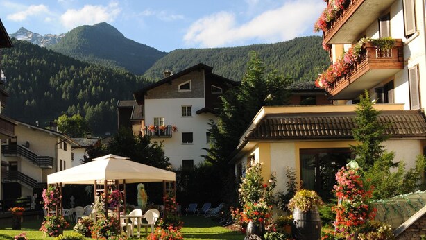 A hotel courtyard with outdoor seating, surrounded by mountain views and lush greenery. - Hotel Posta (Aprica)