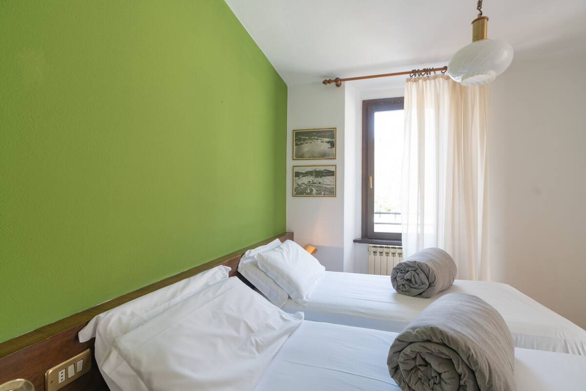 Una habitación con dos camas, una pared verde, una ventana con cortinas y un radiador.