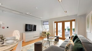 Un salon moderne comprenant un canapé, une table basse, un téléviseur et un coin repas avec une table mise pour deux personnes.