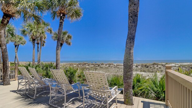 Una terrazza con poltrone relax vista spiaggia, palme e cielo sereno.