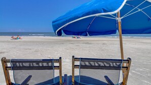 Una spiaggia con due sdraio blu e un ombrellone azzurro.