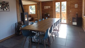 A wooden dining area with a long table and blue chairs, a fireplace, and a view of the outdoors. - Well-being of the old do **** (Ventron)