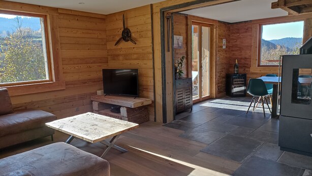 A wooden cabin interior with a television on a wooden stand, a sofa, a dining table, and a kitchen area with a refrigerator. - Well-being of the old do **** (Ventron)
