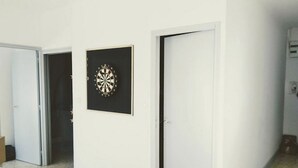 Um corredor com paredes brancas, um alvo de dardos e uma porta fechada.