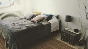 Quarto com cama, mesa de cabeceira, abajur e janela com vista.