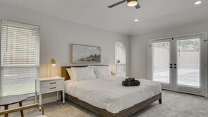 A bedroom with a bed, bedside tables, a ceiling fan, and a large window with blinds. - Gorgeous Sunny Home for Big Groups w/ Private Pool (Garland)