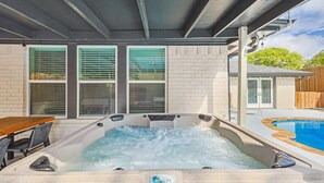 A hot tub under a covered patio with a brick wall and windows. - Gorgeous Sunny Home for Big Groups w/ Private Pool (Garland)