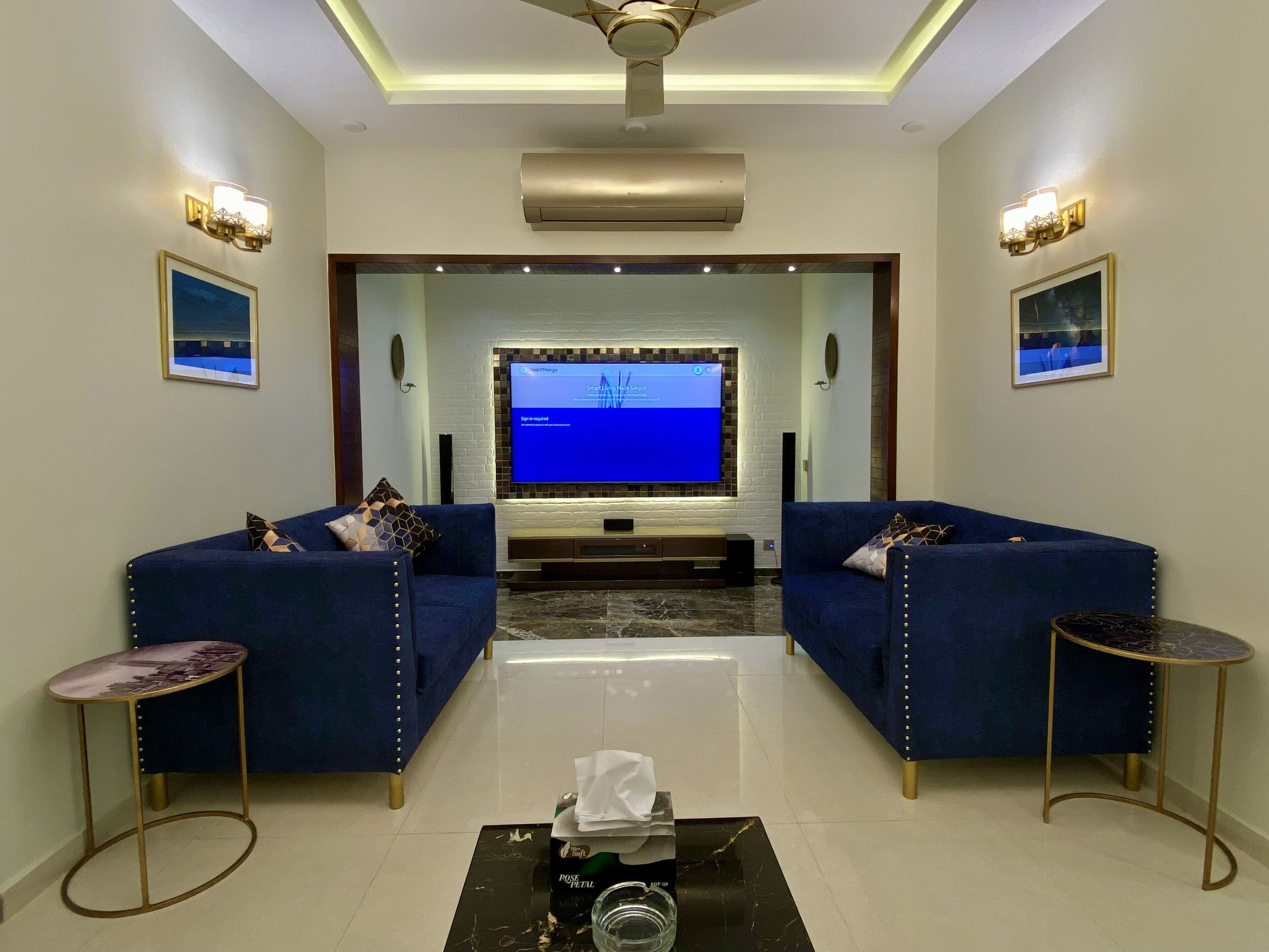 Una sala de estar moderna con dos sofás azules, un televisor de pantalla plana y un ventilador de techo.