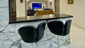 Zona bar moderna con un bancone in marmo, due sgabelli neri e un grande specchio che riflette l'ambiente.