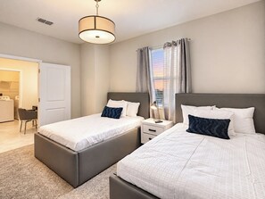 A hotel room with two beds, a desk, a chair, and a window with curtains.