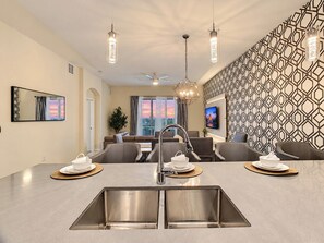 A modern kitchen with a central island, stainless steel sink, and pendant lighting.