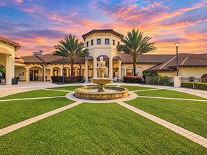 A courtyard with a central fountain, surrounded by palm trees and a building with arched doorways.