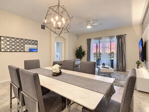 A dining area with a long table, chairs, a chandelier, and a ceiling fan.