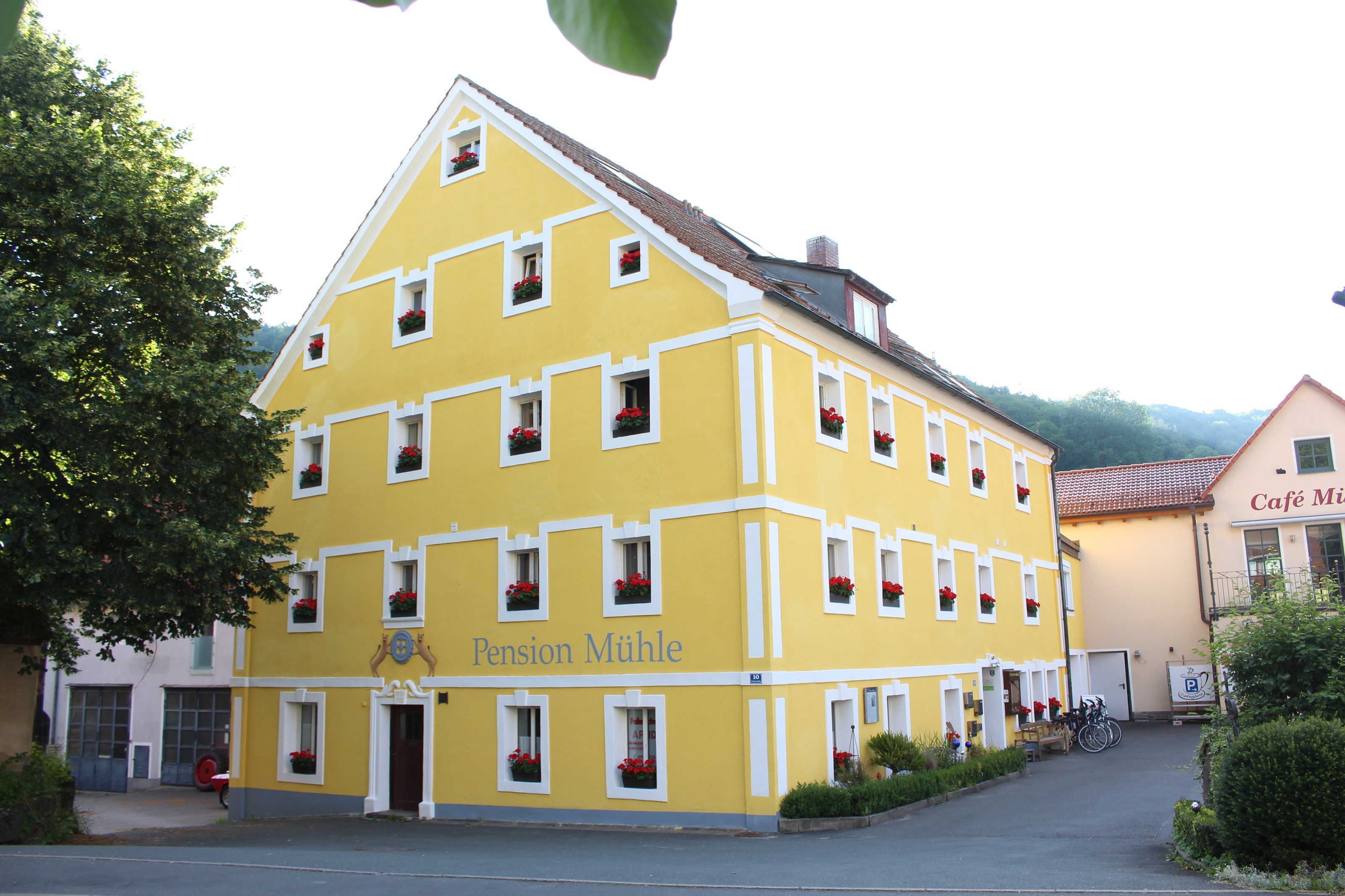 Ein gelbes Gebäude mit mehreren Fenstern, einer Tür und einem Schild mit der Aufschrift 'Pension Mühl'.