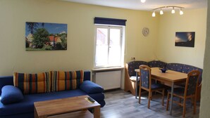 A living room with a sofa, a dining table with chairs, a radiator, and a window with a view of houses.