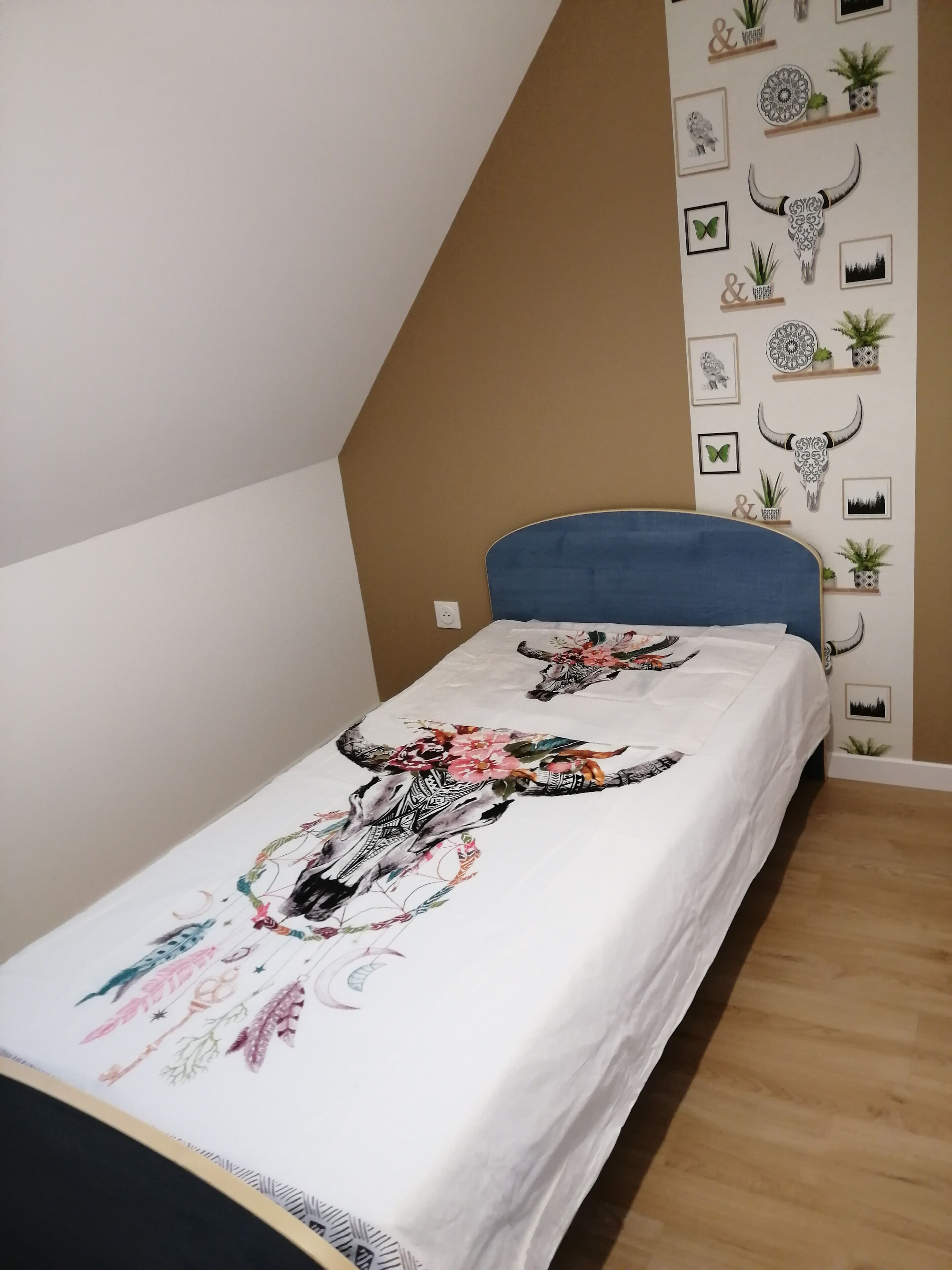 A bedroom with a bed, a sloped ceiling, and a wall decorated with framed pictures and potted plants.