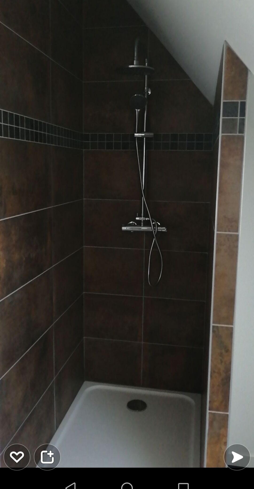 A shower area with dark brown tiles and a white shower base.