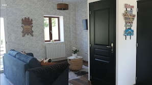 A living room with a blue sofa, a window, a radiator, a decorative wall, and a door with a welcome sign. - Pleasant country cottage in a quiet location (Wirwignes)