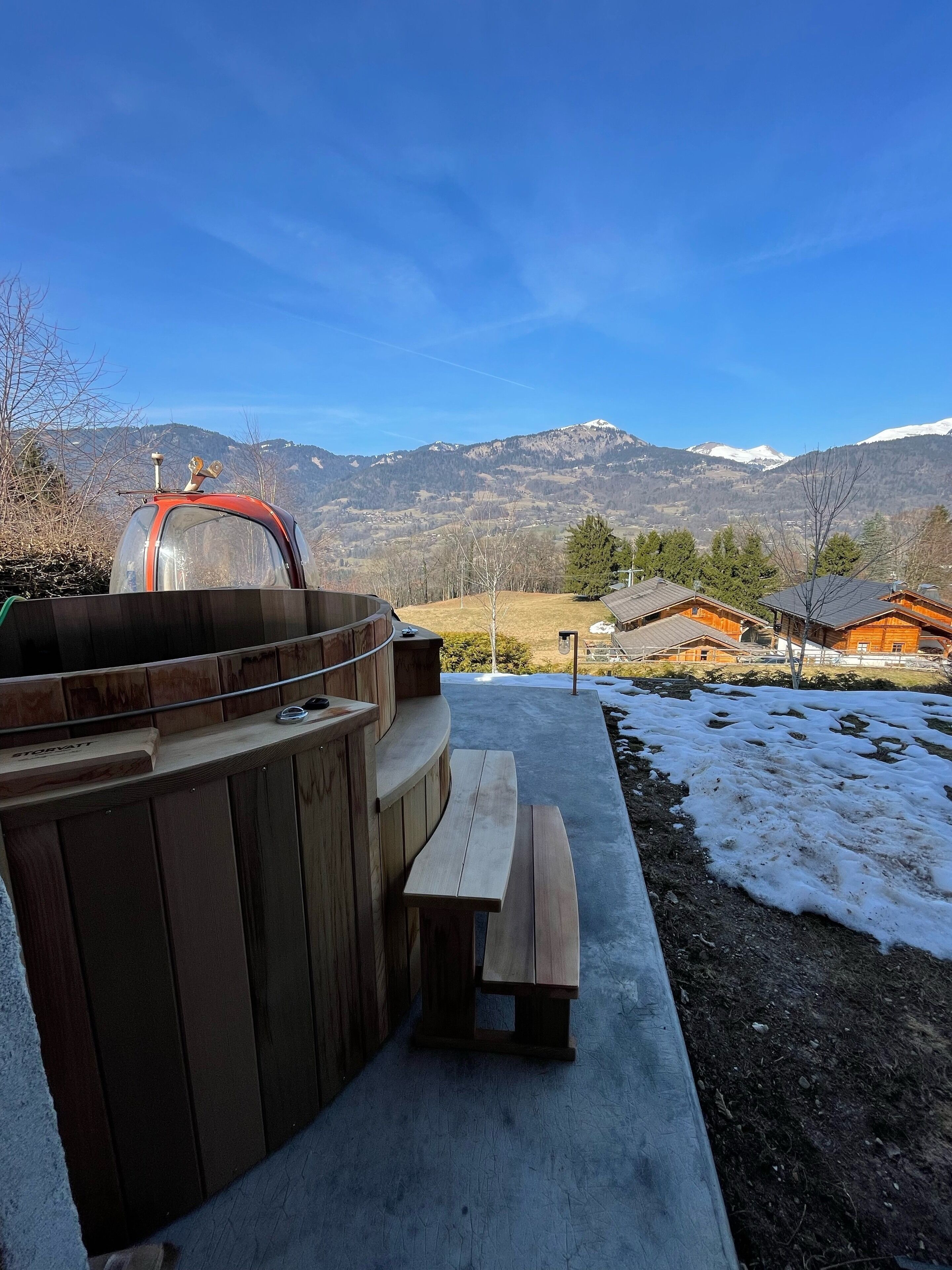 Eine Holzterrasse mit Grill und Picknicktisch, mit Blick auf eine verschneite Landschaft und Berge.