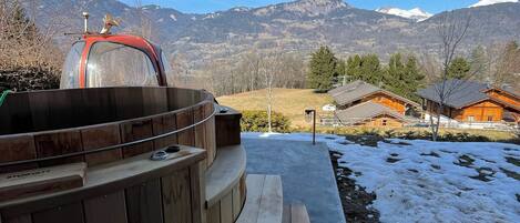 Eine Holzterrasse mit Grill und Picknicktisch, mit Blick auf eine verschneite Landschaft und Berge.