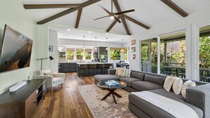 Een ruime woonkamer met een grote grijze hoekbank, een glazen salontafel en een moderne keuken op de achtergrond.