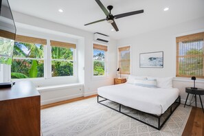 A bedroom with a bed, a desk, a ceiling fan, and windows with blinds. - Surf Hale, Elegant and Luxurious Surf Retreat (Princeville)
