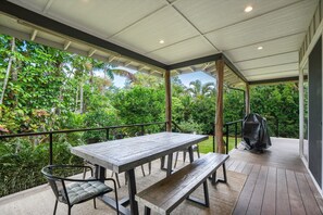 An outdoor patio with a wooden table and chairs, surrounded by lush greenery. - Surf Hale, Elegant and Luxurious Surf Retreat (Princeville)