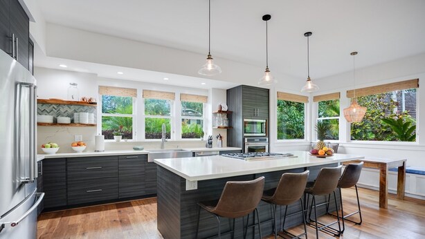 Een moderne keuken met een groot eiland, barkrukken en uitzicht op groen door grote ramen.
