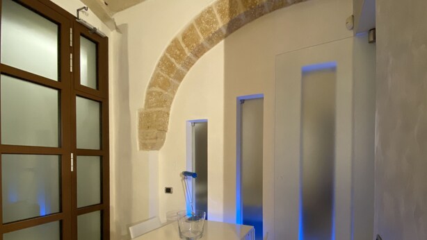 A room with a white table and chairs, a glass pitcher, a stone archway, and a door with frosted glass panels. - Abitazione Tipica (Lecce)