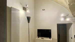 A modern bathroom with a stone ceiling, a radiator, a floor lamp, and a TV on a cabinet. - Abitazione Tipica (Lecce)