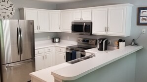 A modern kitchen with white cabinets, stainless steel appliances, a microwave, toaster, and a coffee maker. - Beautiful, 3 br/2 bath condo in Pawleys Island, SC. Minutes from the beach. (Pawleys Island)