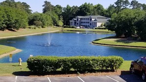 A serene pond with a fountain, surrounded by well-maintained grass and trees. A building with multiple floors is visible in the background. - Beautiful, 3 br/2 bath condo in Pawleys Island, SC. Minutes from the beach. (Pawleys Island)