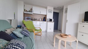 A compact living space with a sofa, a green chair, a small table, a TV, and a kitchenette. - Appartement 2 Pièces Face à la mer (Valras-Plage)