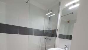 A modern bathroom with a glass shower enclosure, a white sink with a mirror, and a tiled floor. - Appartement 2 Pièces Face à la mer (Valras-Plage)