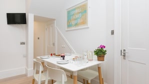 A dining area with a white table set for four, a flat-screen TV mounted on the wall, and a framed quote above the table. - Summer Salt – St Ives – Sleeps 4 – Parking – Outside Space (St Ives)