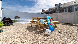 Une terrasse avec une table en bois, une planche de surf gonflable bleue et un ballon de foot.
