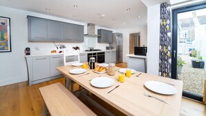 Une cuisine moderne avec des meubles gris, une table à manger en bois dressée pour deux personnes et une grande fenêtre donnant sur un jardin.