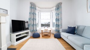 Un salon moderne avec un téléviseur à écran plat posé sur un meuble blanc, un canapé bleu clair, une table basse ronde et un tapis blanc.