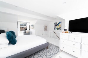 Une chambre moderne avec un grand lit, une commode blanche, un téléviseur à écran plat et une fenêtre donnant sur l’extérieur.