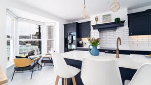 Una cocina moderna con una isla grande, armarios oscuros y vistas a un puerto deportivo a través de amplios ventanales.