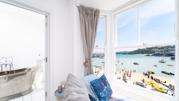 Habitación con vista a la playa, una bañera y una ventana con cortinas.