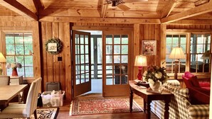 Ein Holzblockhaus-Interieur mit Essbereich, einem Wohnzimmer mit karierter Couch, einem Tisch mit Blumenvase und einem Deckenventilator.