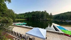 Eine Terrasse am See mit Stühlen und Tisch, beschattet durch ein Zelt, umgeben von einem ruhigen See und dichtem Wald.