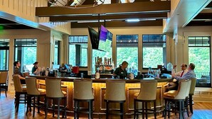 Eine Bar mit einer langen Theke, mehreren Barhocker und einem Barkeeper.