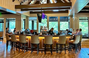 A bar area with a long counter, multiple bar stools, and a bartender.