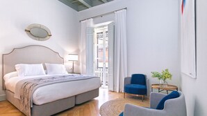 Une chambre à coucher avec un lit, deux chaises, une petite table et une fenêtre avec des rideaux.