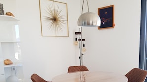 A dining area with a round table, four brown chairs, a tall floor lamp, and wall art. - Porticcio, Superb air-conditioned T2, panoramic view of the Gulf of Ajaccio (Albitreccia)