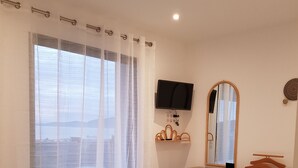 A bedroom with a bed, a dresser, a TV, a mirror, and a window with sheer curtains. - Porticcio, Superb air-conditioned T2, panoramic view of the Gulf of Ajaccio (Albitreccia)