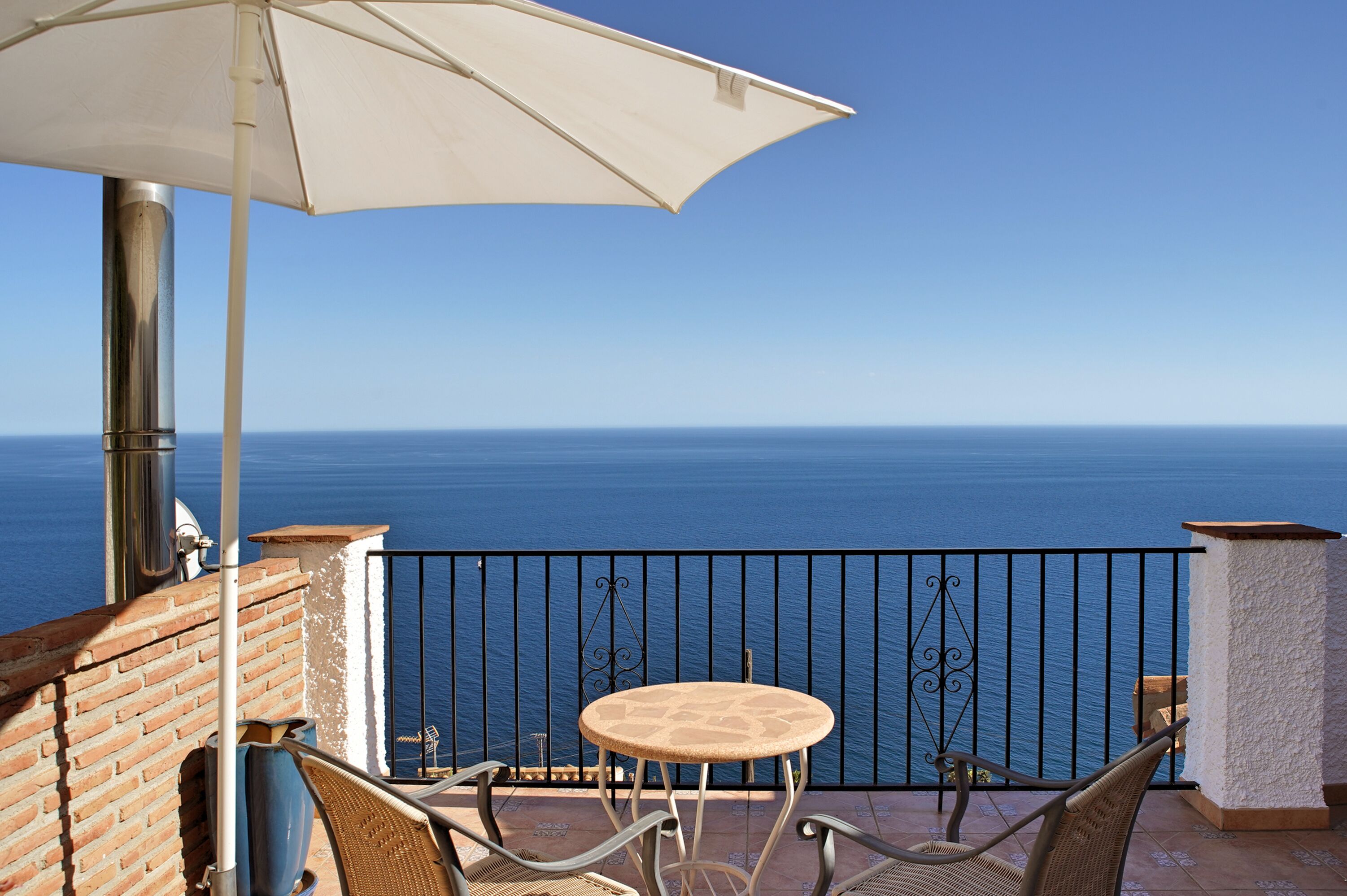Een balkon met een tafel en stoelen, een witte parasol en uitzicht op de zee.